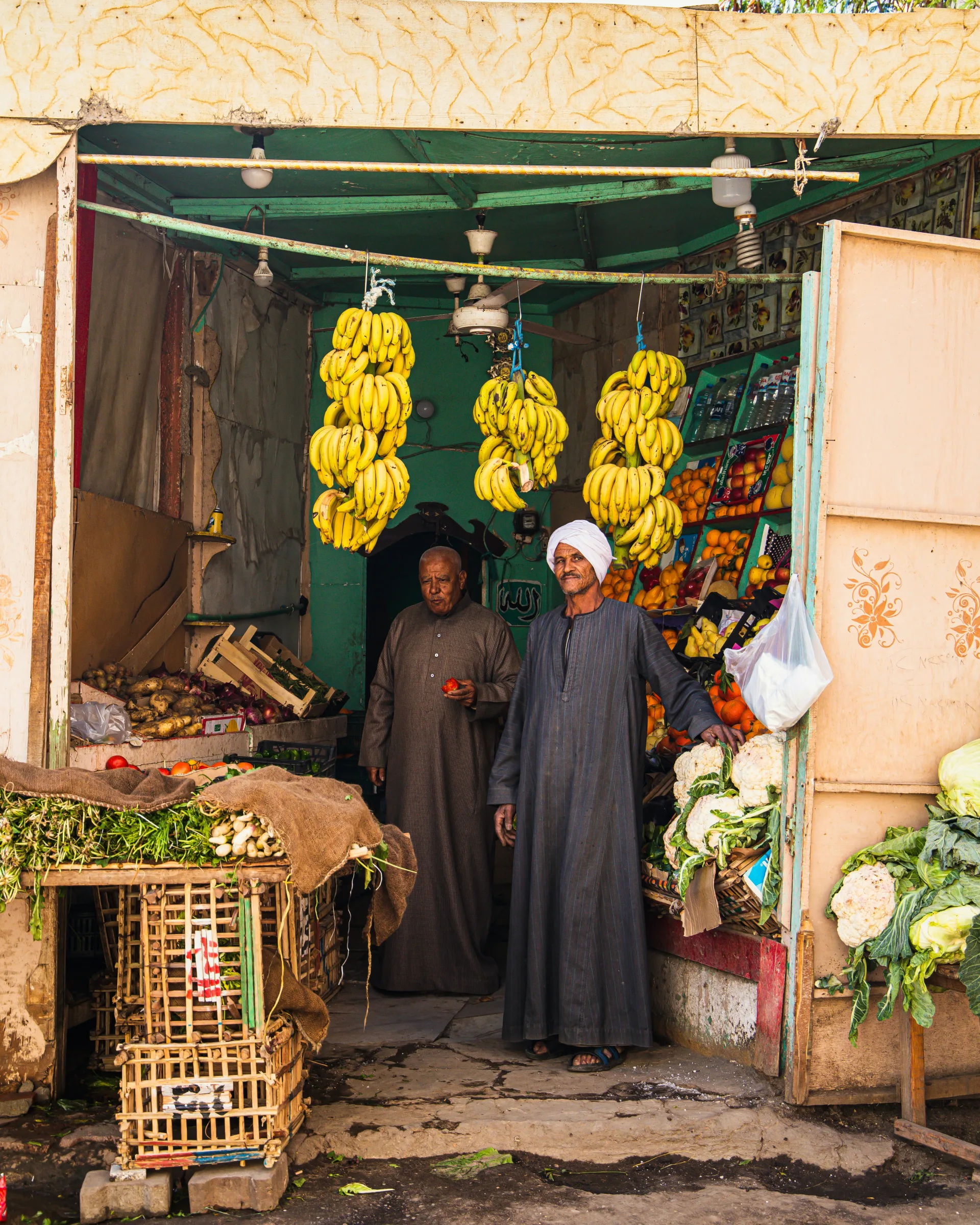 Fruit sellers standing beneath bunches of bananas at an Egyptian market stall