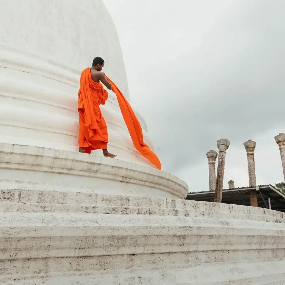 Buddhist monk walking beside a white stupa in Sri Lanka